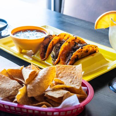 Three cheese and birria tacos served with birria broth, tortilla chips, and a cocktail.