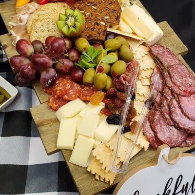 A charcuterie board with assorted cheeses, salami, crackers, olives, dried and fresh fruits.