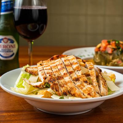 Chicken salad on a table with red wine, beer bottle, and a dish in the background.