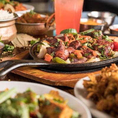 Grilled marinated lamb chunks with veggies in a pan, surrounded by other dishes.