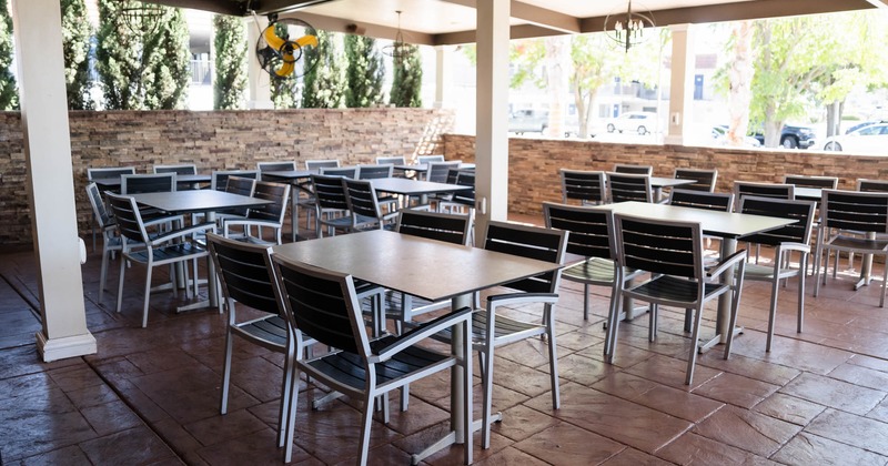 Outdoor seating area with tables, chairs, stone flooring and walls, and hanging chandeliers