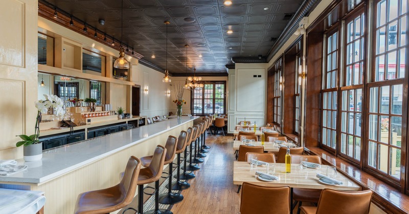 Interior, bar with stools, tables for four ready for guests, low hanging chandeliers