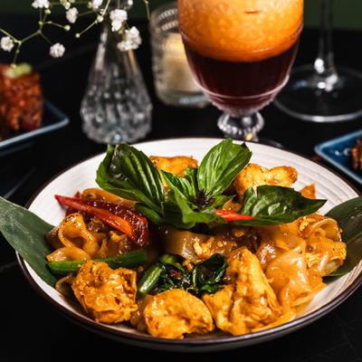 Drunken noodles with tofu, garnished with basil leaves.