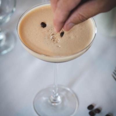 A hand garnishing an espresso martini with coffee beans.