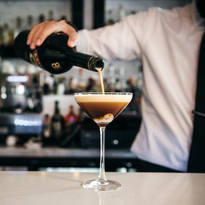Bartender topping espresso martini with creamy liqueur.