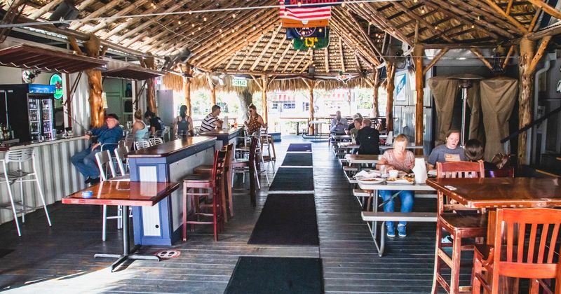 Exterior, guests dining in covered seating area with tables for dining and a bar