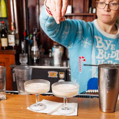 A bartender garnishing two cocktails in coupe glasses with shredded coconut.