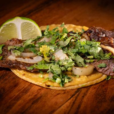 Steak taco with onions, cilantro, and lime.