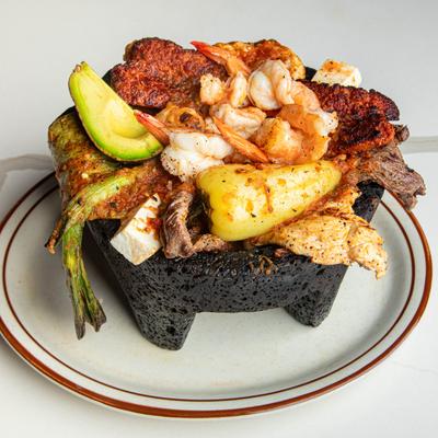 Molcajete served in a hot lava rock bowl on a white plate.
