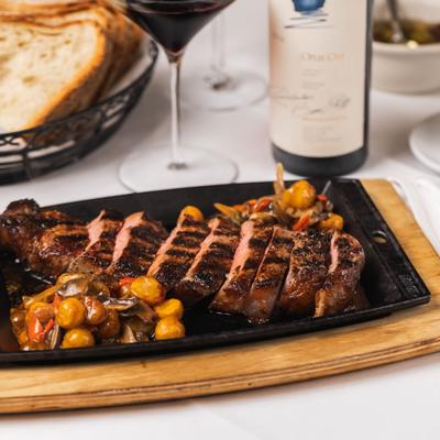 Grilled steak with vegetables served on a hot plate with red wine and bread.