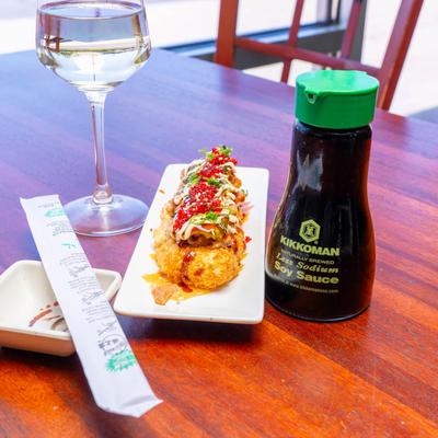 A plate of sushi on a table beside a glass of wine and a bottle of soy sauce.