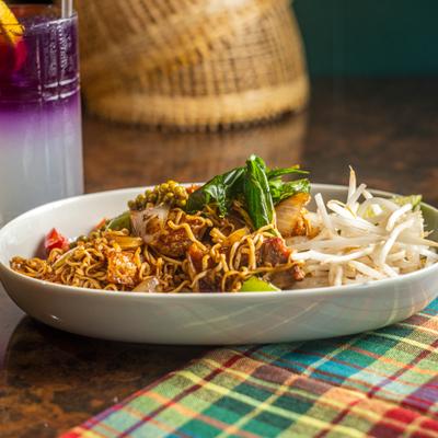 Stir-fried Thai noodles with bean sprouts beside a layered purple and white drink.