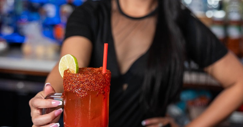 A bartender holding a michelada drink
