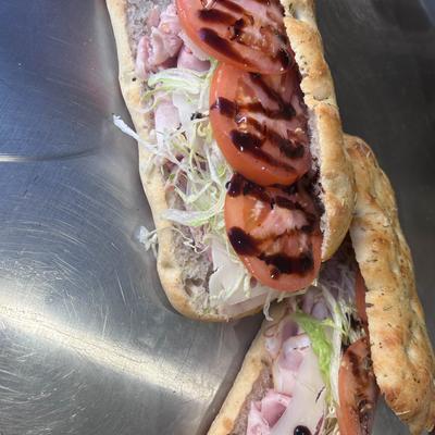 Two flatbread sandwiches with ham, lettuce, and tomato drizzled.