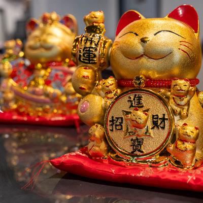 A close-up of a golden lucky cat figurine holding a coin on a red cushion.