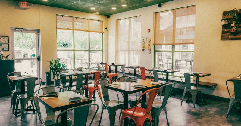 Modern restaurant interior with wooden tables, metal chairs, and large windows