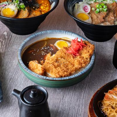 Breaded chicken curry bowl beside ramen dishes.