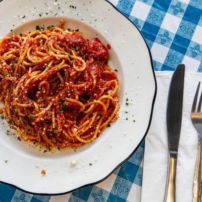 Amatriciana pasta on a white plate, served on a blue checkered table with utensils.