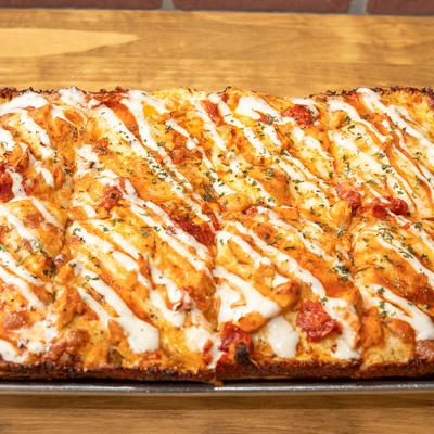 Square pizza with chicken, cheese, chilis, and ranch drizzle.