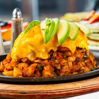 Skillet breakfast dish with diced potatoes, topped with scrambled eggs and avocado.