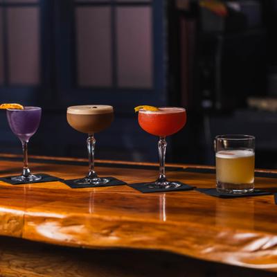 Colorful cocktails lined up on a wooden counter.