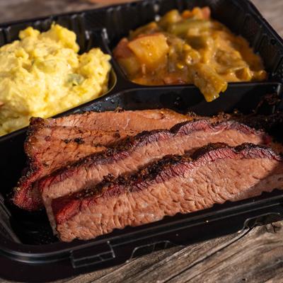 Smoked BBQ brisket with potato salad and smothered green beans in a takeout container.
