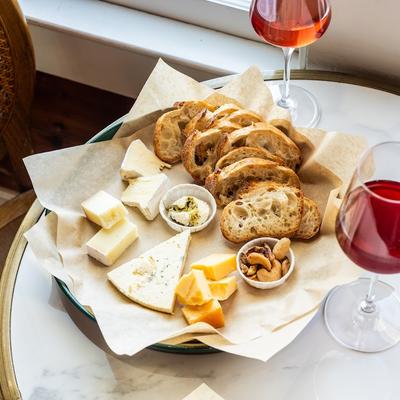 Cheese plate with bread slices, nuts, and glasses of wine.