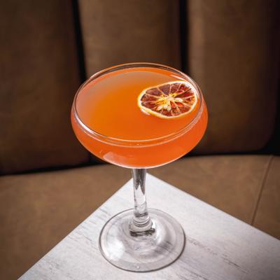 Orange cocktail with citrus slice on light table.