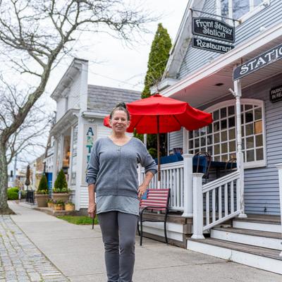 Exterior with restaurant signboard, person looking into the camera and smiling.