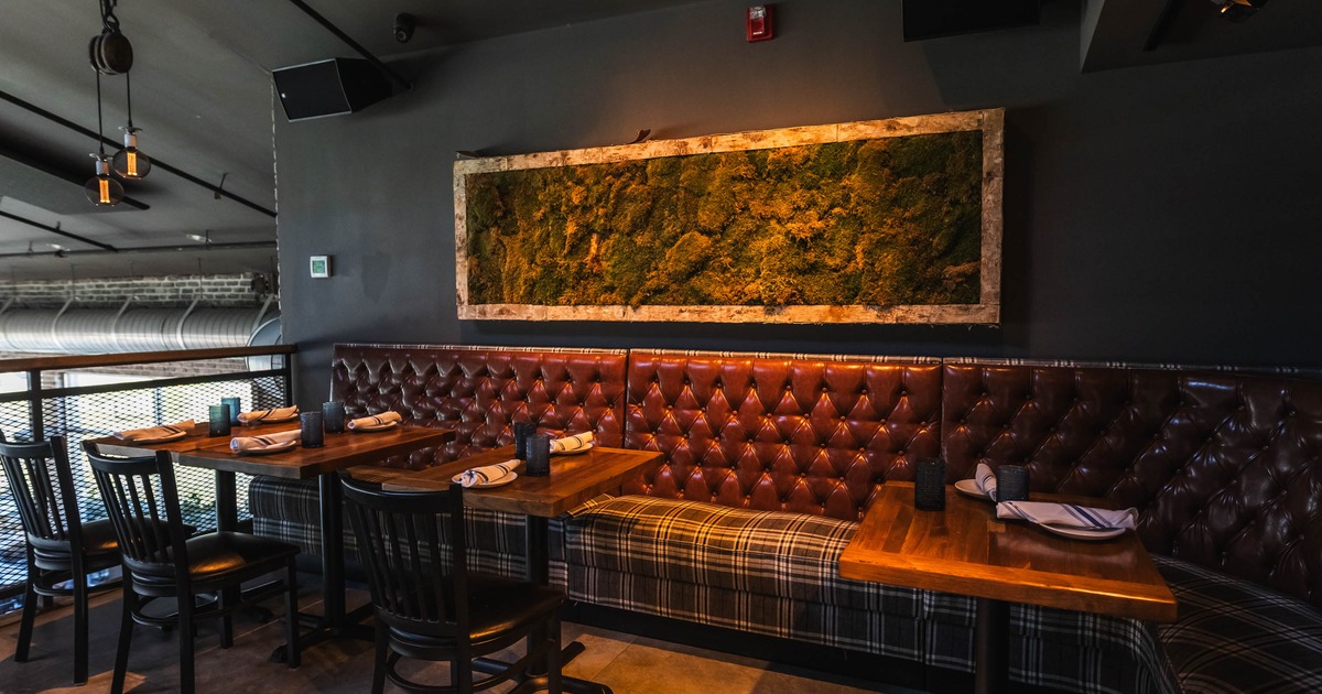Restaurant interior with leather booth seating, wooden tables, moss wall art, and soft lighting