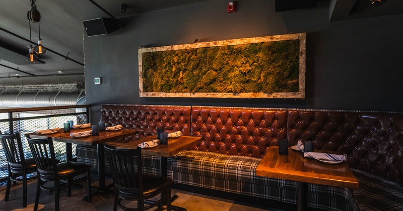 Restaurant interior with leather booth seating, wooden tables, moss wall art, and soft lighting