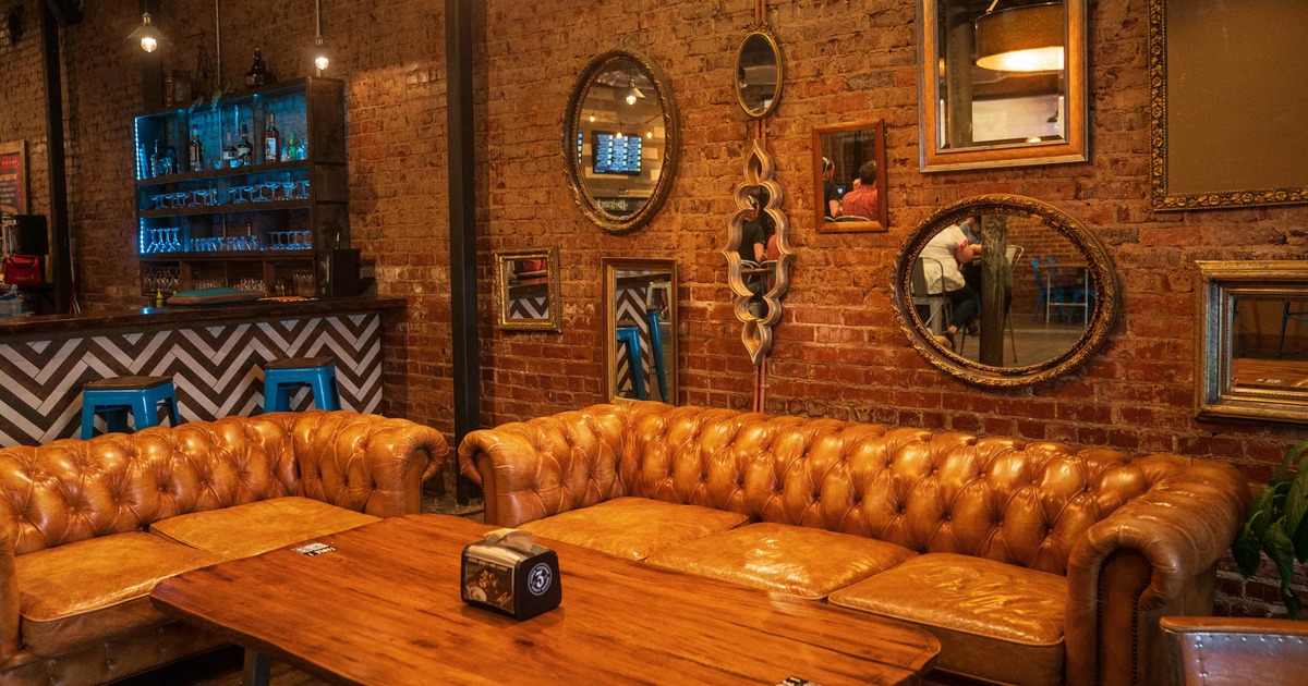 Interior, button tufted sofa seating, vintage mirrors on the wall, and the bar