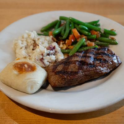Grilled steak, with veggies, potato salad, and a bun.