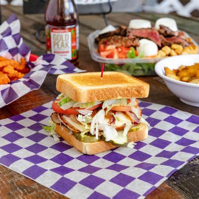 Grilled Club Sandwich served alongside a drink in the bottle and other dishes.