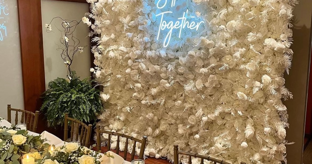 Wedding backdrop featuring a white floral wall and a light blue neon sign