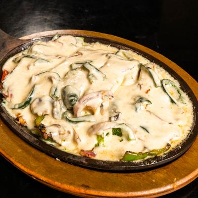 Fajitas con queso served sizzling in a cast-iron skillet on a wooden base.