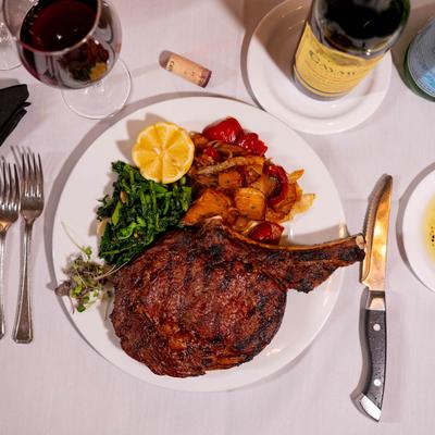 Bone in rib eye steak served with cooked vegetables, spinach, and wine.