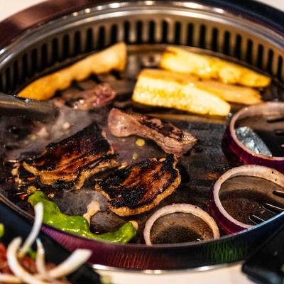Korean BBQ grill featuring sizzling marinated meats, sliced onions, and vegetables.