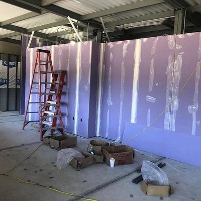 A room with a purple wall is being constructed, some cardboard boxes and a ladder are in it