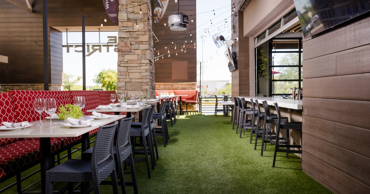 Outdoor dining area with tables set for meals, bar seating, and string lights overhead