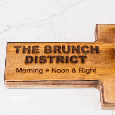A wooden sign with the text The Brunch District, and the slogan Morning, Noon and Right.