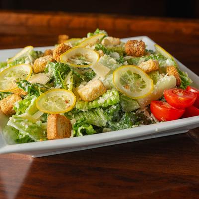 Caesar Salad plate sits on a shiny wooden table, close up.
