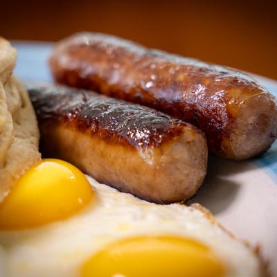 Sausage links served with fried eggs on plate, close up.