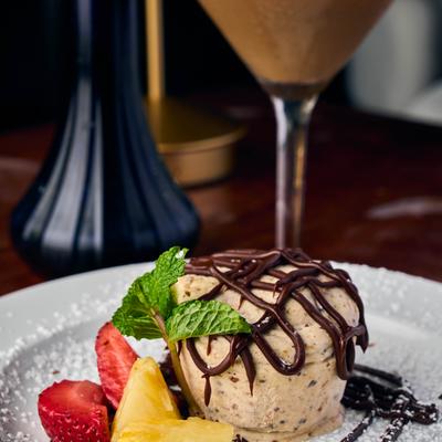 Ice cream dessert drizzled with chocolate sauce, garnished with fruit and mint.