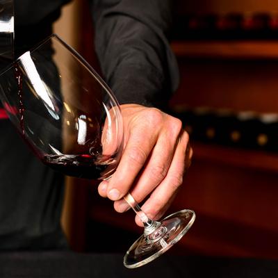A sommelier pouring red wine from a bottle into a glass, hand close up.