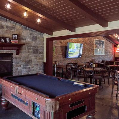 Bar interior with brick walls, pool table, stone fireplace, and wooden tables.