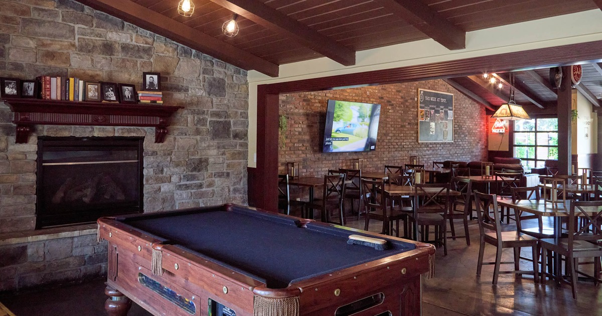 Bar interior with brick walls, pool table, stone fireplace, and wooden tables