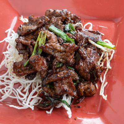 Mongolian beef served over crispy fried rice noodles on a red plate.