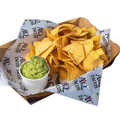 Tortilla chips served in a paper lined cardboard boat with guacamole.