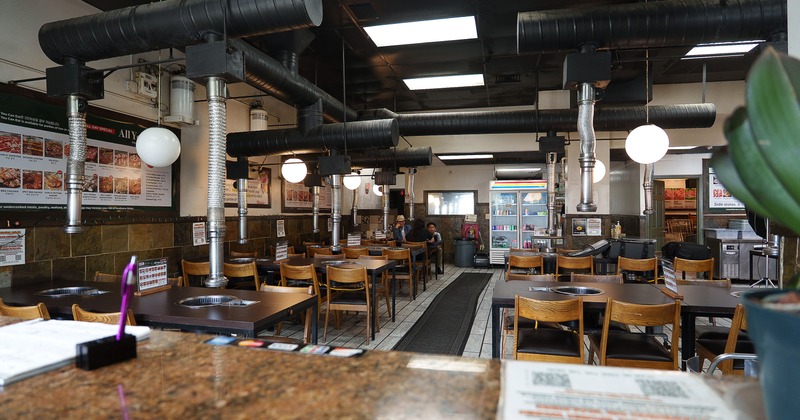 Spacious Korean BBQ restaurant with tables with built-in grills and overhead ventilation pipes